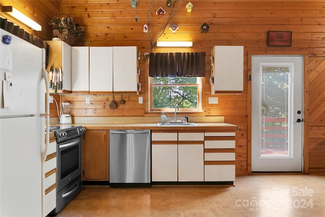 kitchen with appliances with stainless steel finishes, white cabinets, sink, and wooden walls