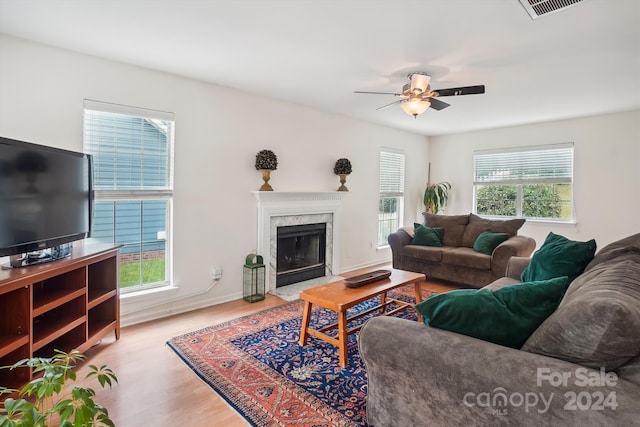 living room featuring light wood-type flooring, ceiling fan, a high end fireplace, and a wealth of natural light