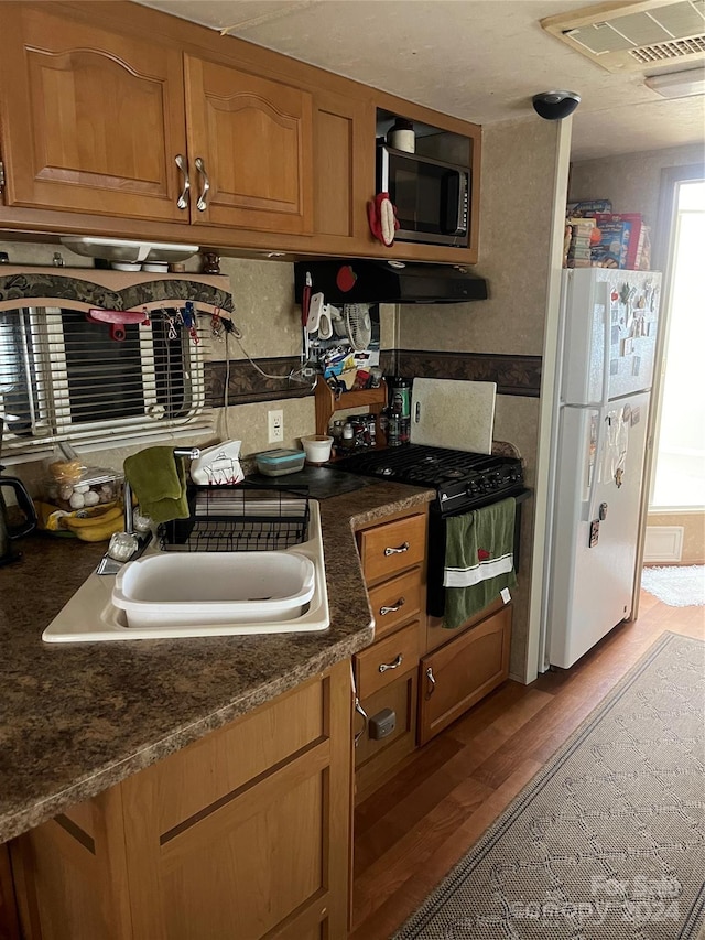 kitchen with light hardwood / wood-style flooring, dark stone countertops, white fridge, and black range with gas cooktop