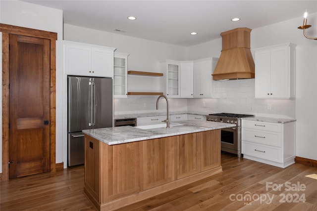 kitchen with white cabinets, an island with sink, high end appliances, sink, and hardwood / wood-style flooring