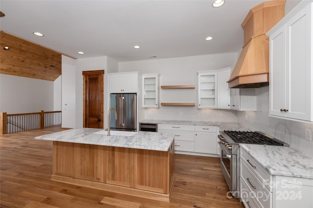 kitchen featuring light stone countertops, premium appliances, white cabinetry, an island with sink, and decorative backsplash