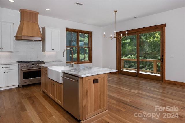 kitchen featuring sink, white cabinetry, a kitchen island with sink, stainless steel appliances, and custom range hood