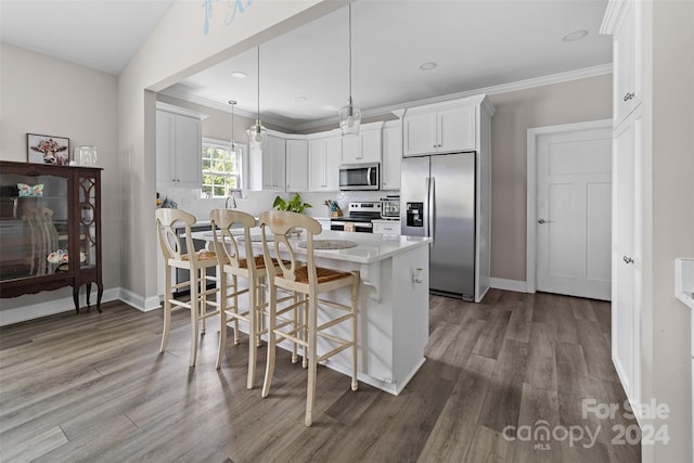 kitchen featuring appliances with stainless steel finishes, a breakfast bar area, hardwood / wood-style floors, pendant lighting, and white cabinetry