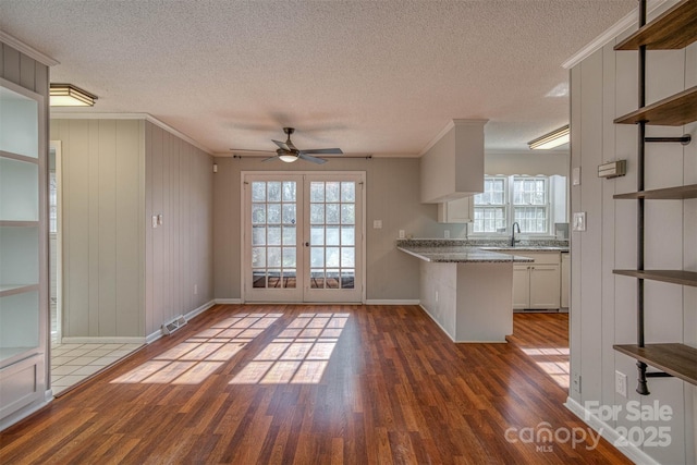 unfurnished living room with crown molding, plenty of natural light, dark hardwood / wood-style floors, and french doors