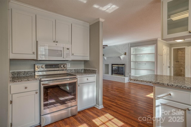 kitchen with light hardwood / wood-style flooring, a textured ceiling, white cabinets, a brick fireplace, and stainless steel electric stove