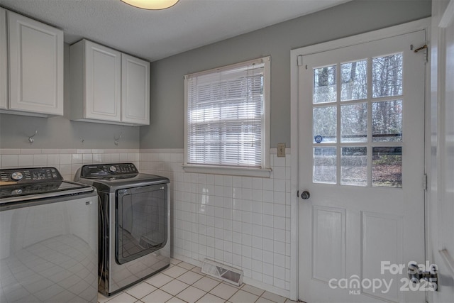 washroom with light tile patterned floors, tile walls, cabinets, independent washer and dryer, and a textured ceiling