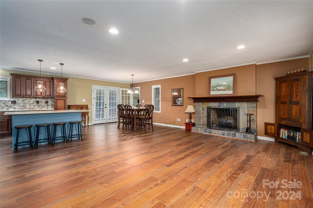 living room featuring wood-type flooring, a stone fireplace, a textured ceiling, and crown molding