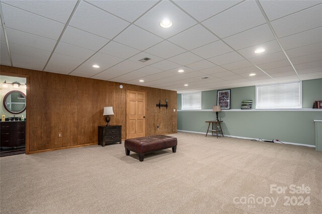 living area with wooden walls, light colored carpet, a healthy amount of sunlight, and a paneled ceiling