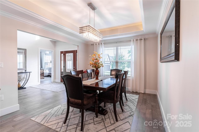 dining space with crown molding, a notable chandelier, a tray ceiling, and light wood-type flooring