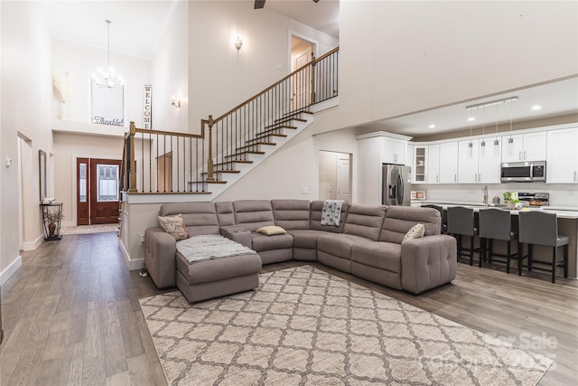 living room featuring sink, a notable chandelier, light wood-type flooring, and a towering ceiling