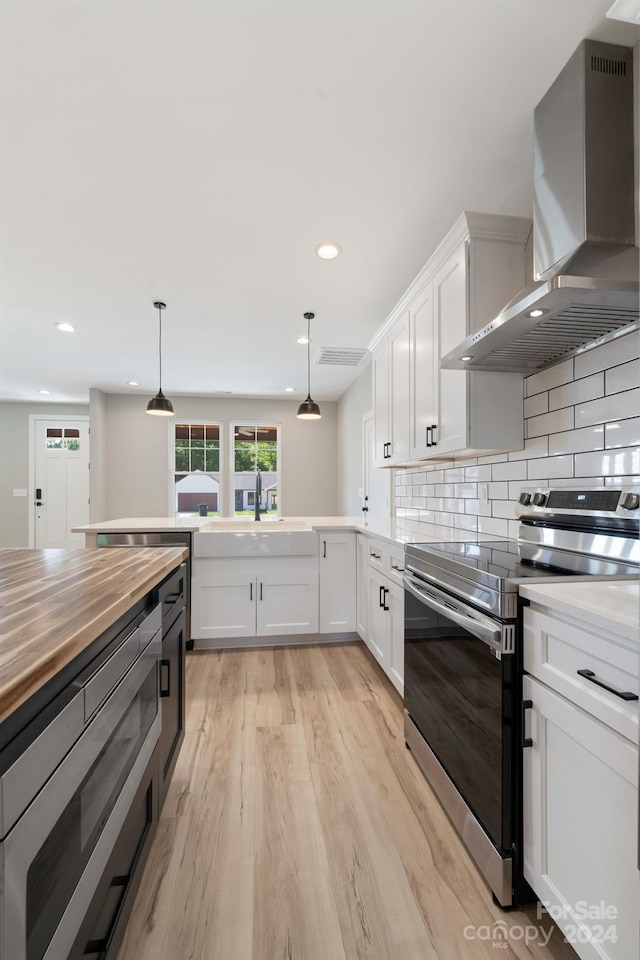 kitchen with wall chimney exhaust hood, decorative backsplash, appliances with stainless steel finishes, decorative light fixtures, and white cabinetry