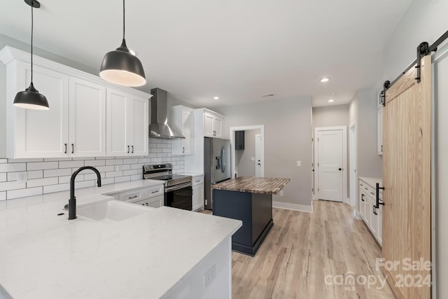 kitchen with appliances with stainless steel finishes, sink, wall chimney range hood, white cabinets, and a center island