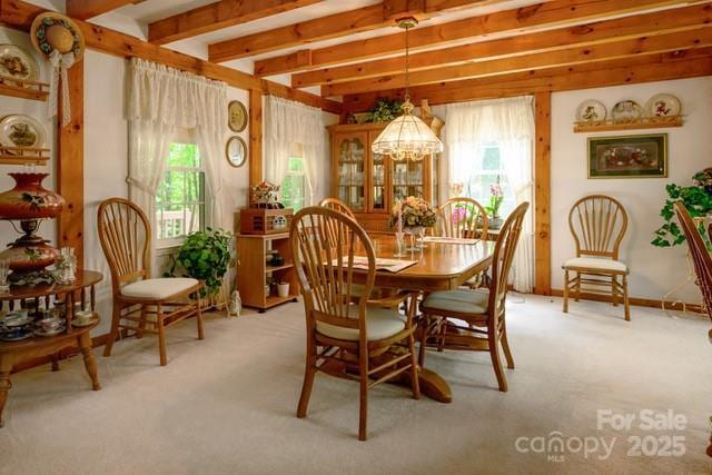 carpeted dining space featuring beam ceiling and an inviting chandelier