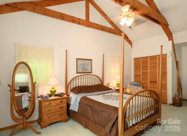 carpeted bedroom with ceiling fan, lofted ceiling with beams, and a closet