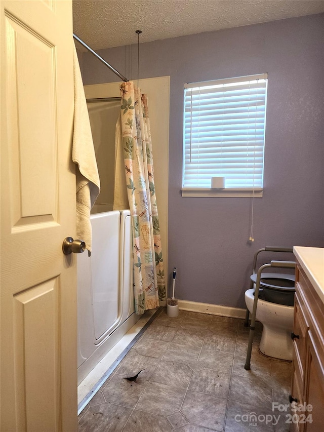 bathroom featuring toilet, vanity, walk in shower, and a textured ceiling