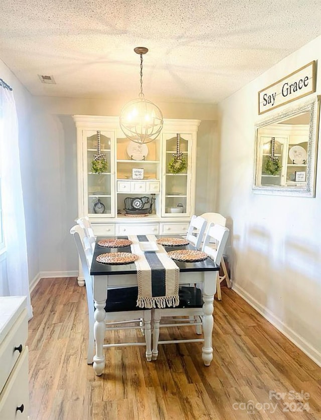 dining space with a textured ceiling, an inviting chandelier, and light hardwood / wood-style floors