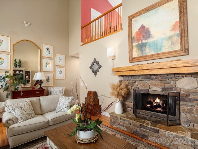 living room with a stone fireplace, hardwood / wood-style floors, and a towering ceiling