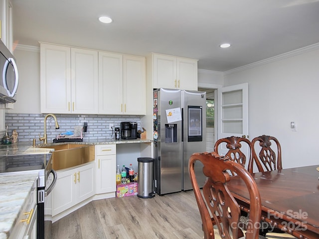 kitchen with appliances with stainless steel finishes, sink, white cabinets, light stone counters, and crown molding