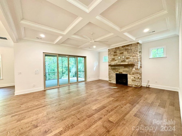 unfurnished living room featuring ceiling fan, a stone fireplace, wood-type flooring, and a wealth of natural light