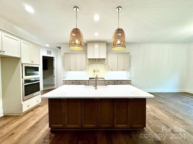 kitchen with decorative light fixtures, an island with sink, stainless steel appliances, and hardwood / wood-style floors