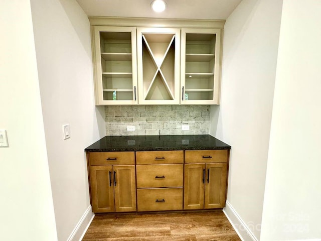 bar featuring dark stone counters, decorative backsplash, and wood-type flooring