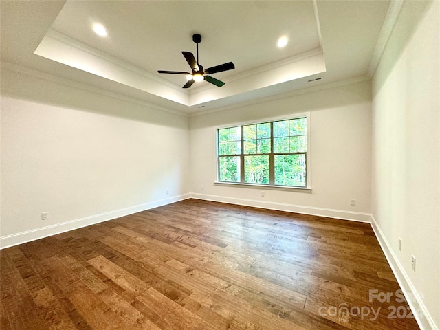 empty room featuring crown molding, a tray ceiling, dark wood-type flooring, and ceiling fan