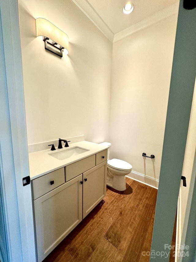 bathroom featuring wood-type flooring, vanity, crown molding, and toilet