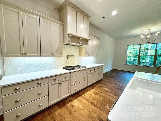 kitchen with light stone counters, stainless steel gas cooktop, an inviting chandelier, hardwood / wood-style floors, and ornamental molding