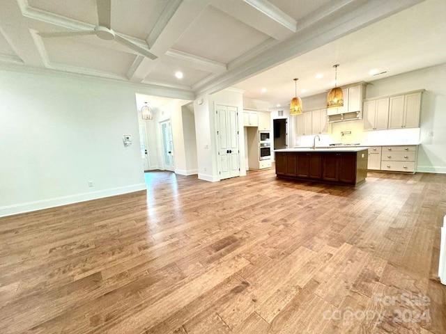 interior space featuring ceiling fan, beamed ceiling, hanging light fixtures, a center island with sink, and hardwood / wood-style floors