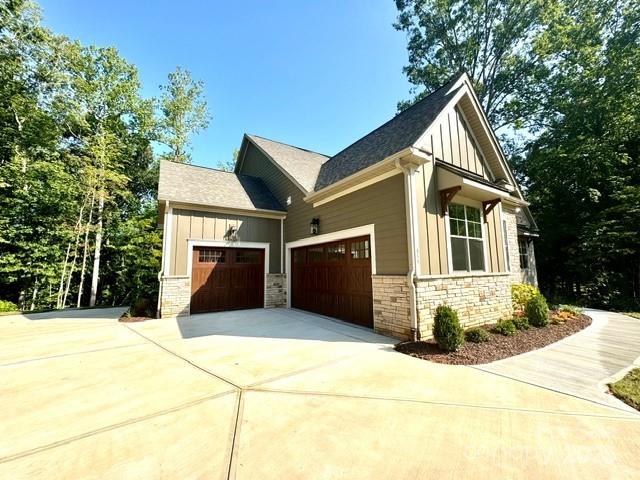 view of side of property with a garage, stone siding, board and batten siding, and concrete driveway