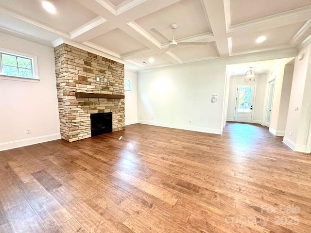 unfurnished living room featuring coffered ceiling, wood finished floors, and a stone fireplace