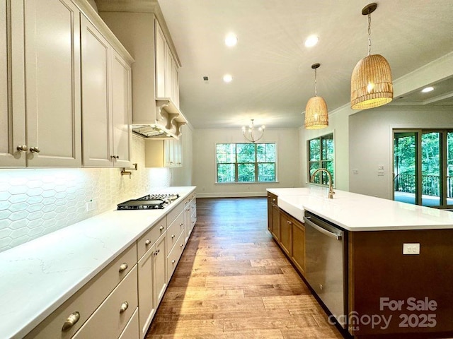 kitchen with light wood finished floors, tasteful backsplash, appliances with stainless steel finishes, a sink, and an island with sink