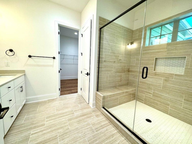 bathroom with a spacious closet, a shower stall, vanity, and baseboards