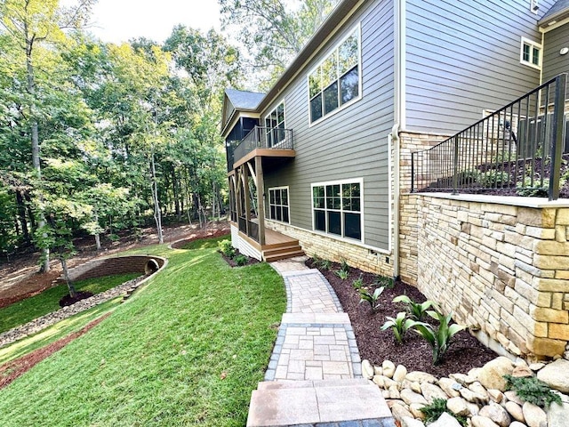 view of property exterior featuring stone siding, a yard, and a balcony