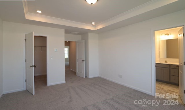 unfurnished bedroom featuring crown molding, ensuite bath, a closet, a tray ceiling, and a spacious closet