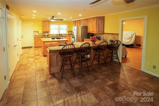 kitchen featuring ceiling fan, ornamental molding, a kitchen breakfast bar, and freestanding refrigerator