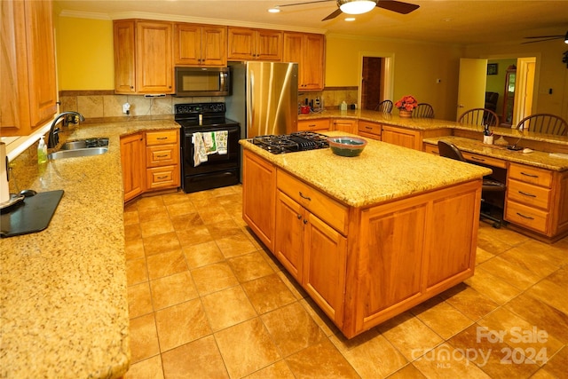 kitchen with ceiling fan, a kitchen island, appliances with stainless steel finishes, light stone counters, and a sink