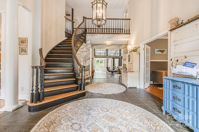 foyer entrance featuring a notable chandelier, a towering ceiling, and decorative columns