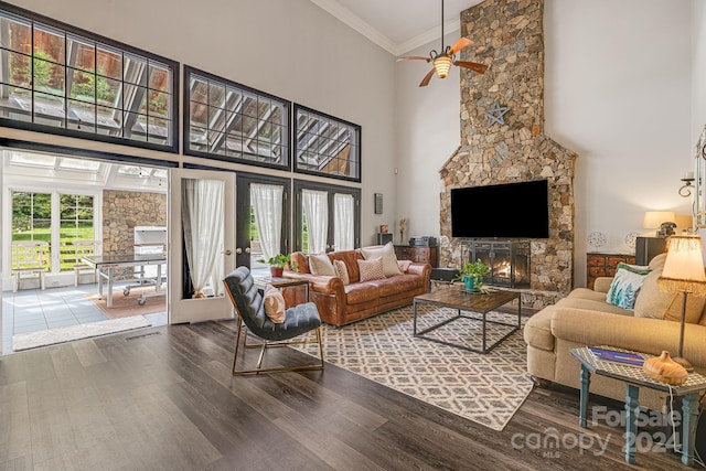 living room with a wealth of natural light, a towering ceiling, wood-type flooring, a fireplace, and crown molding