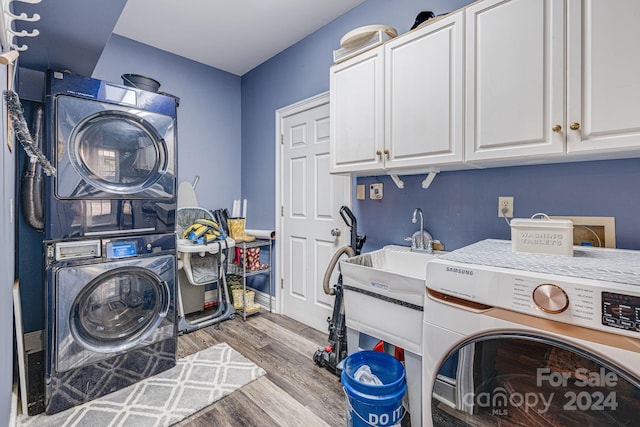 laundry room featuring light wood-type flooring, stacked washer and clothes dryer, and cabinets