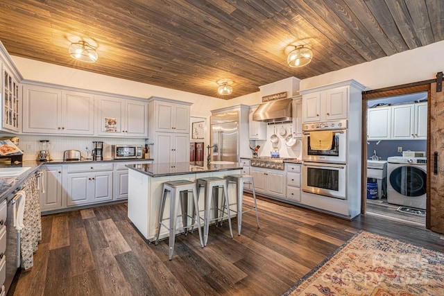 kitchen with washer / dryer, a kitchen bar, appliances with stainless steel finishes, wall chimney exhaust hood, and a center island