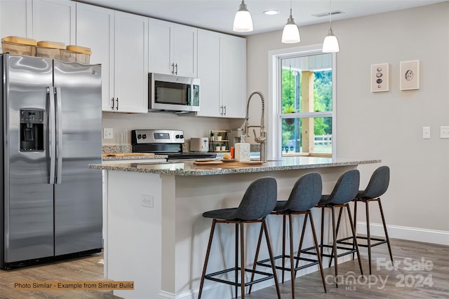 kitchen featuring stainless steel appliances, white cabinetry, light stone counters, light wood-type flooring, and pendant lighting