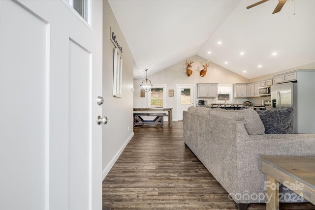 living room with lofted ceiling, recessed lighting, ceiling fan with notable chandelier, dark wood-type flooring, and baseboards