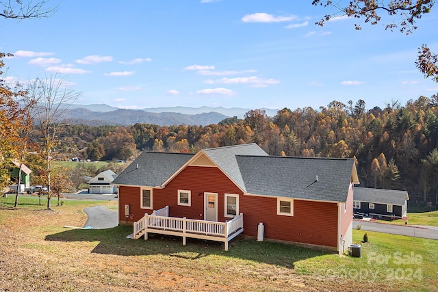 rear view of property with a deck with mountain view, central AC, a yard, and roof with shingles