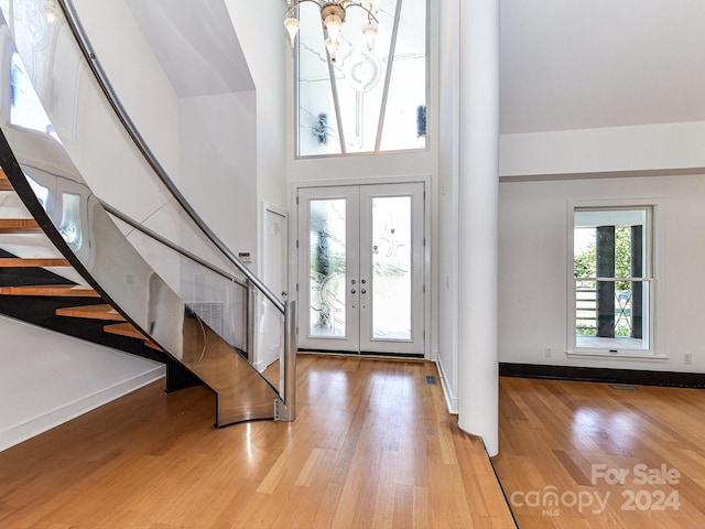 foyer with light hardwood / wood-style floors, a chandelier, french doors, and a towering ceiling