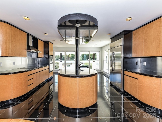 kitchen with backsplash, wall chimney range hood, a kitchen island with sink, stainless steel built in fridge, and black electric cooktop