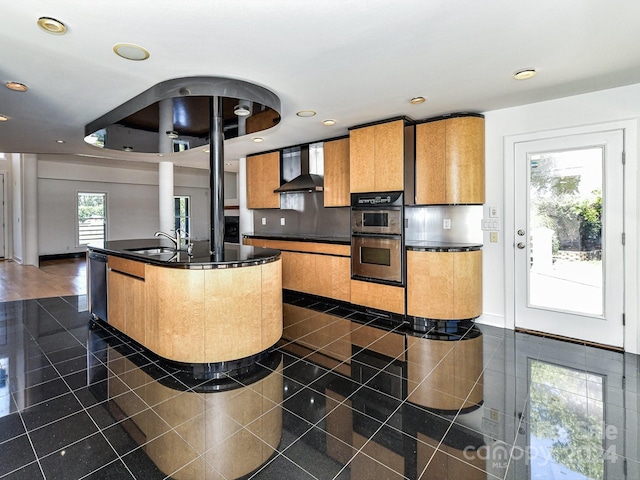 kitchen featuring wall chimney range hood, stainless steel appliances, an island with sink, sink, and backsplash