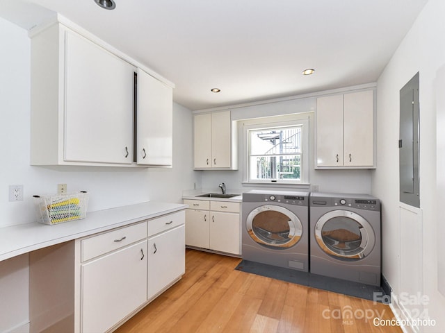 laundry area with light hardwood / wood-style floors, independent washer and dryer, cabinets, electric panel, and sink