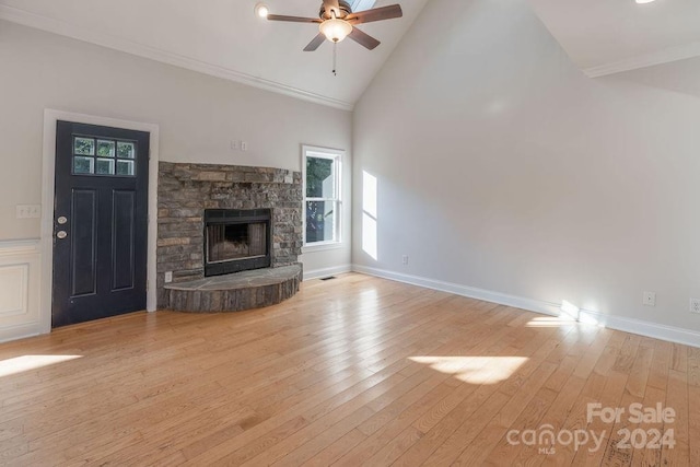 unfurnished living room featuring ceiling fan, high vaulted ceiling, crown molding, a fireplace, and light wood-type flooring