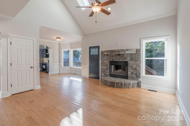 unfurnished living room with light wood-type flooring, ceiling fan, crown molding, high vaulted ceiling, and a stone fireplace